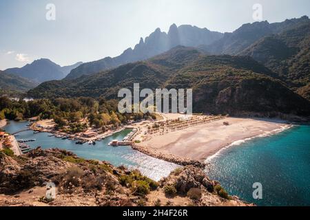 Der Strand und das türkisfarbene Mittelmeer führen zum Hafen von Porto an der Westküste Korsikas mit Bergen dahinter Stockfoto