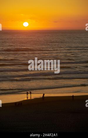 Pazifik Oregon Coast Sonnenuntergang vertikal. Menschen, die den Sonnenuntergang in Cannon Beach, Oregon, genießen, während die Brandung am Strand aufgeht. Usa. Stockfoto