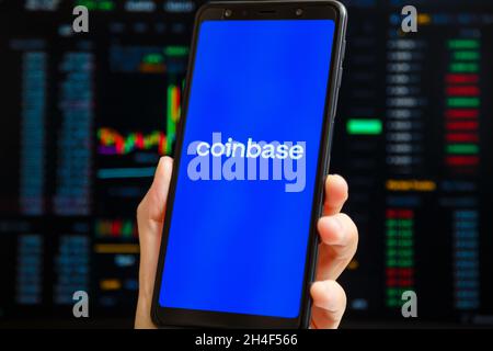Ukraine, Odessa - Oktober, 9 2021: Hand hält Handy mit Coinbase App läuft auf Smartphone-Bildschirm mit Trading-Seite im Hintergrund. Coinbase ist Ame Stockfoto