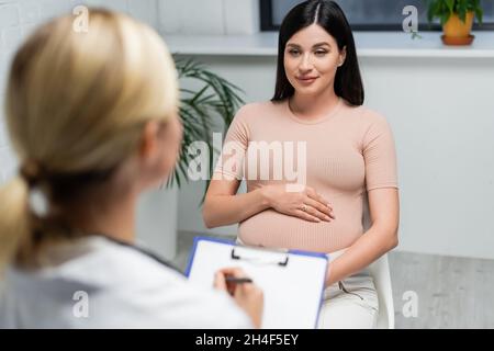 Schwanger Frau in der Nähe verschwommen Arzt schreiben Rezept im Sprechzimmer Stockfoto