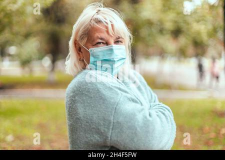 Blonde Frau trägt eine schützende Gesichtsmaske und einen warmen Kaschmirschal im Park im Freien während der Quarantäne einer Coronavirus-Pandemie. Kopieren, leerer Speicherplatz Stockfoto