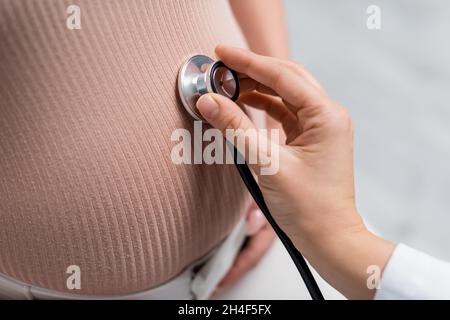 Beschnittene Ansicht einer Schwangeren und eines Arztes, die ihren Bauch mit Stethoskop untersuchen Stockfoto