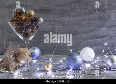 weihnachtskegel und -Spielzeug in einem martini-Glas, eine ungewöhnliche Komposition aus goldenen Tannenzapfen, Neujahrslicht und einer schönen Quappe Blume ist ein stilvoller Look Stockfoto