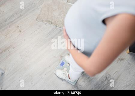 Beschnittene Ansicht einer Schwangeren, die zu Hause auf einer Personenwaage steht Stockfoto