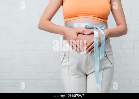 Teilansicht der Schwangeren Frau, die Herzzeichen in der Nähe Satinband auf dem Bauch Stockfoto