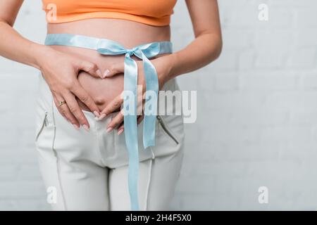 Teilansicht der Schwangeren Frau macht Liebe Zeichen auf Bauch mit Satinschleife Stockfoto