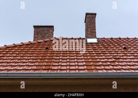Nasses rotes Ziegeldach an einem regnerischen Herbsttag. Leichter Regen fällt auf das Dach eines Hauses Stockfoto