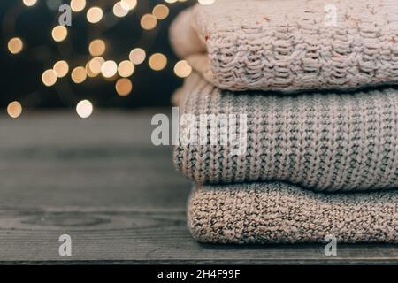 Nahaufnahme eines Stapels dickgestrickter Pullover auf Holzbrettern und Bokeh-Lichtern im Hintergrund. Stockfoto