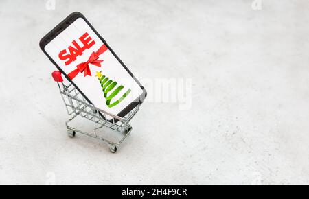 Mobiltelefon mit Verkaufsschild in einem Mini-Warenkorb vor weißem Hintergrund mit Kopierplatz. Stockfoto