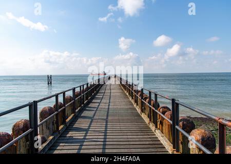 Blick auf das Meer über die Strandpromenade eines Wellenbrechers und einer Anlegestelle an der Küste der Stadt Westkapelle in den Niederlanden mit einem einzigen Schiff, das vorbeifährt Stockfoto