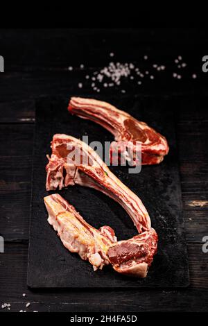 Frische, rohe Lammrippchen. Halal-Fleisch. Rohes Fleisch. Lammkarree auf dunklem rustikalem Hintergrund. Salz und Gewürze. Halal Food Stillleben. Vertikale Aufnahme Stockfoto