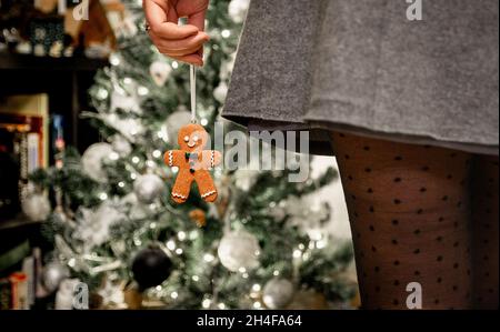 Nahaufnahme einer jungen Frau mit Rock und Strumpfhose mit Punktmuster, die vor dem weihnachtsbaum steht und mit Lebkuchenmännchen verziert ist Stockfoto