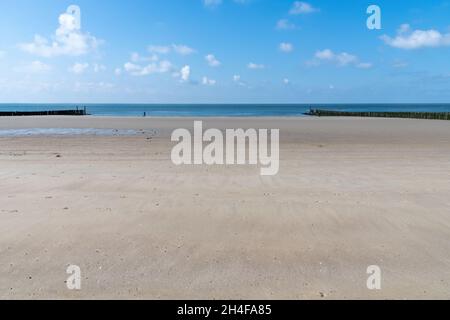 Panoramablick über den breiten Strand von Westkapelle, Niederlande, zwischen den Wellenbrechern links und rechts des Bildes; ein Angler Stockfoto