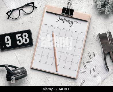 Januar Kalender flach lag. Draufsicht des Januarkalenders auf der Tabelle. Mobiltelefon mit Flip-Clock auf dem Bildschirm und Kalender auf hellem Hintergrund. Stockfoto