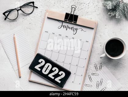 Januar Kalender flach lag. Draufsicht des Januarkalenders auf der Tabelle und des Jahres 2022 auf dem Display des Mobiltelefons. Stockfoto