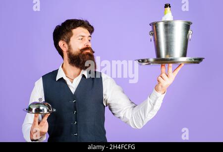 Professioneller Kellner in Uniform mit Serviertablett und Weinkühler. Restaurant serviert. Butler mit Restaurantcloche und Eiskübel mit Flasche Stockfoto