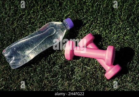 Gesunde ausgewogene Lebensweise. Pflegen Sie den Wasserhaushalt im Körper während des Trainings. Langhanteln und Flasche auf grünem Gras. Sport-Werkzeug und Ausrüstung. Hanteln in Stockfoto