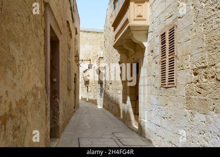 Typische Mdina Straße. Schmale mittelalterliche Straße von Mdina, auch als "stille Stadt" bekannt, gepflastert mit Steinplatten und mit gelben Kalkstein Mauern umgeben. Stockfoto