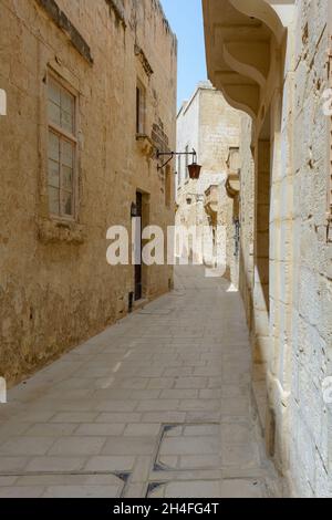 Typische Mdina Straße. Schmale mittelalterliche Straße von Mdina, auch als "stille Stadt" bekannt, gepflastert mit Steinplatten und mit gelben Kalkstein Mauern umgeben. Stockfoto