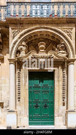 Historische verzierte grüne Holztür in einem Steineingang in Mdina, Malta. Mit Steinbögen Schnitzereien oben. Architektonisches Thema. Stockfoto