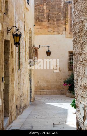 Typische Mdina Straße. Schmale mittelalterliche Straße von Mdina, auch als "stille Stadt" bekannt, gepflastert mit Steinplatten und mit gelben Kalkstein Mauern umgeben. Stockfoto