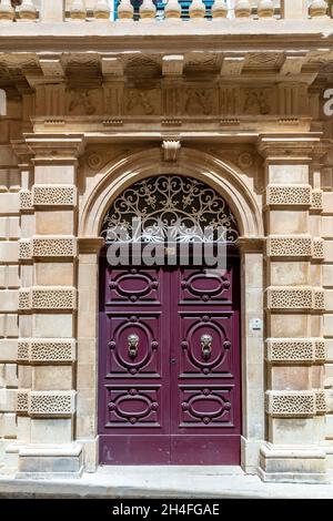 Burgunder Holzbogentür mit vergoldeten Türknockern mit Löwenköpfen verziert. Vintage Eingangstüren in Mdina, Malta. Stockfoto