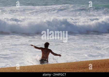 Sportlicher, atraktiver Mann (keine Erkennbarkeit), der in die Wellen läuft, Nazare, Portugal Stockfoto