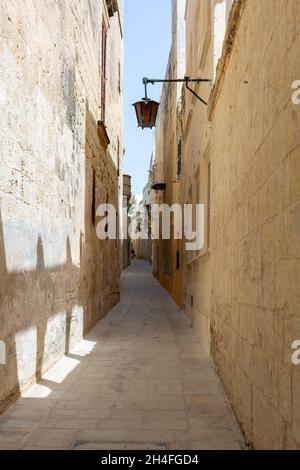 Typische Mdina Straße. Schmale mittelalterliche Straße von Mdina, auch als "stille Stadt" bekannt, gepflastert mit Steinplatten und mit gelben Kalkstein Mauern umgeben. Stockfoto