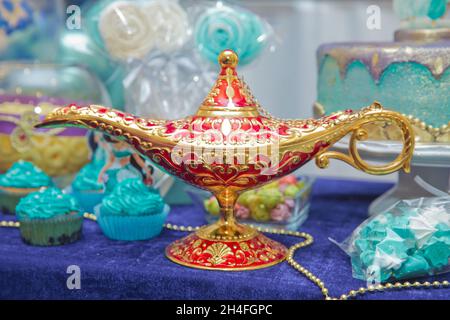 Aladdin Lampe der Wünsche auf dem Tisch. Aladdins magische Genie-Lampe in Rot und Gold auf blauem Hintergrund. Antike goldfarbene Öllampe mit Rost dargestellt Stockfoto