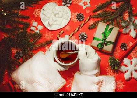 Die Hände des weihnachtsmannes halten eine heiße Tasse Tee. Spielzeug und Geschenke für Neujahr und Weihnachten. Stockfoto