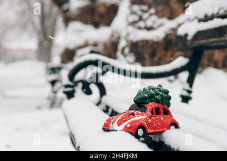 Nahaufnahme eines roten Spielzeugautos mit selektivem Fokus auf der schneebedeckten Parkbank. Stockfoto