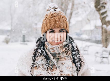 Portrait einer niedlichen jungen Frau mit Schneeflocken im Haar, die im verschneiten Park steht. Stockfoto