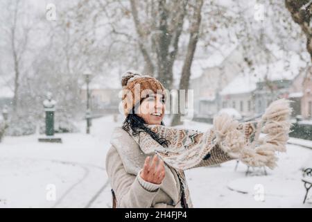 Porträt einer schönen jungen Frau in stilvoller Winterkleidung, die im verschneiten Park steht. Stockfoto