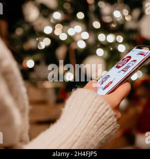 Nahaufnahme der Hand, die das Mobiltelefon vor dem Bokeh-Licht auf dem weihnachtsbaum hält. Stockfoto