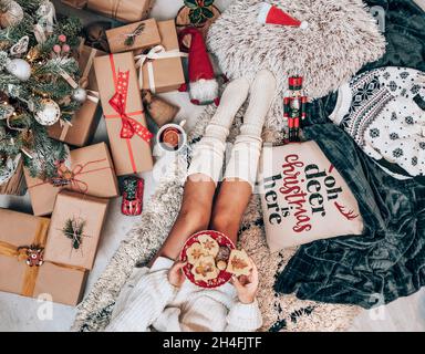 Foto über dem Kopf einer Frau, die am geschmückten Weihnachtsbaum sitzt und Kekse isst Stockfoto