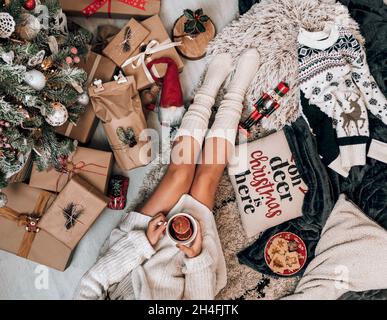 Foto über dem Kopf einer Frau, die an einem geschmückten Weihnachtsbaum sitzt und eingewickeltes Geschenk hält. Stockfoto