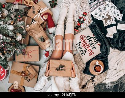 Foto über dem Kopf einer Frau, die an einem geschmückten Weihnachtsbaum sitzt und eingewickeltes Geschenk hält. Stockfoto