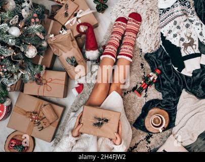 Foto über dem Kopf einer Frau, die an einem geschmückten Weihnachtsbaum sitzt und eingewickeltes Geschenk hält. Stockfoto