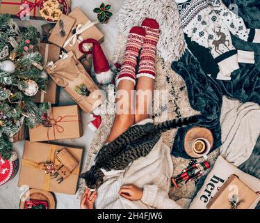 Foto über dem Kopf einer Frau, die am geschmückten Weihnachtsbaum sitzt und eine Katze streichelt Stockfoto