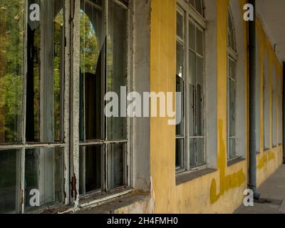 Langer Gang entlang des alten verlassenen Gebäudes mit hohen französischen Fenstern mit kaputten Gläsern. Stockfoto