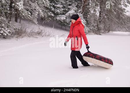 Mädchen in einer roten Jacke ziehen Schlauch in verschneiten Wald. Hohe Qualität Stockfoto