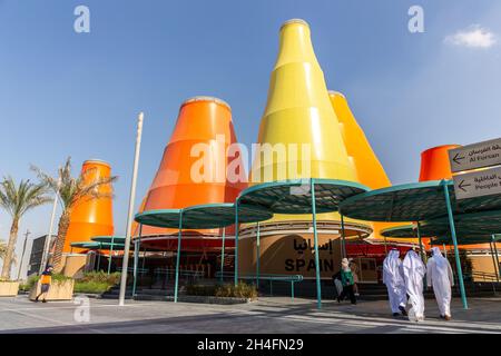 Dubai, VAE, 27.10.2021. Spanien nationaler Pavillon auf der Expo 2020 Dubai, mit orangefarbenen und gelben Türmen und Männern in Kanuras beim Betreten des Gebäudes. Stockfoto