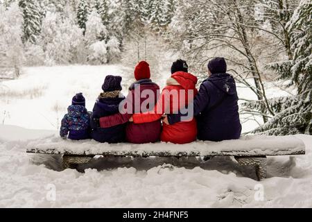 Eine große Familie sitzt auf einer Bank im Winterwald Stockfoto