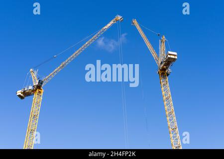 Zwei gelbe Baukräne erstrecken sich an einem sonnigen Tag in Großbritannien in den blauen Himmel auf einem Grundstück in Greenwich, London Stockfoto