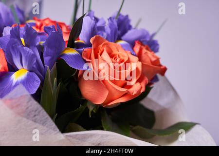 Ein farbenfroher Blumenstrauß aus orangefarbenen Rosen und lila Iris. Auf einem hellen Hintergrund, Seitenansicht. Das Konzept des Urlaubs. Hochwertige Fotos Stockfoto