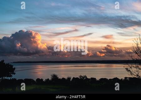 Beeindruckende wabennde Kumuluswolken in der Dämmerung am Horizont entlang und spiegeln sich im Meer. Die Wolken werden durch das goldene, rote Leuchten der Sonne hervorgehoben Stockfoto