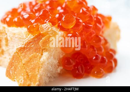 Roter Kaviar auf einer Brotscheibe auf dem weißen Hintergrund in Nahaufnahme Stockfoto