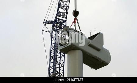 Fernansicht eines Krans, der einen Generator auf einer Windkraftanlage mit dem Himmel im Hintergrund errichtet Stockfoto