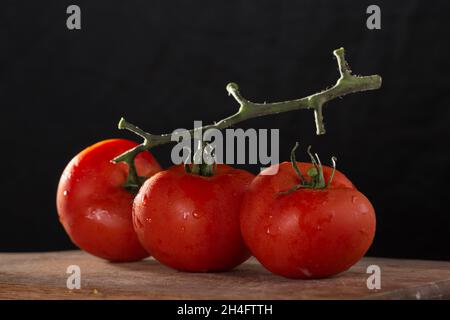 Drei Weintomaten, auf Holzbrett, vor einem schwarzen Hintergrund platziert Stockfoto