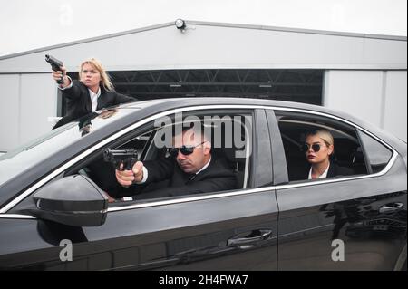 Professionelle bewaffnete Team von weiblichen und männlichen Bodyguards schießen und schützen eine VIP-Prominenten Person in der Auto-Limousine. Bodyguard und VIP Person Security Pro Stockfoto